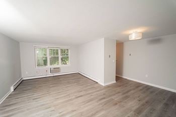A living room with wood floors and white walls and a window